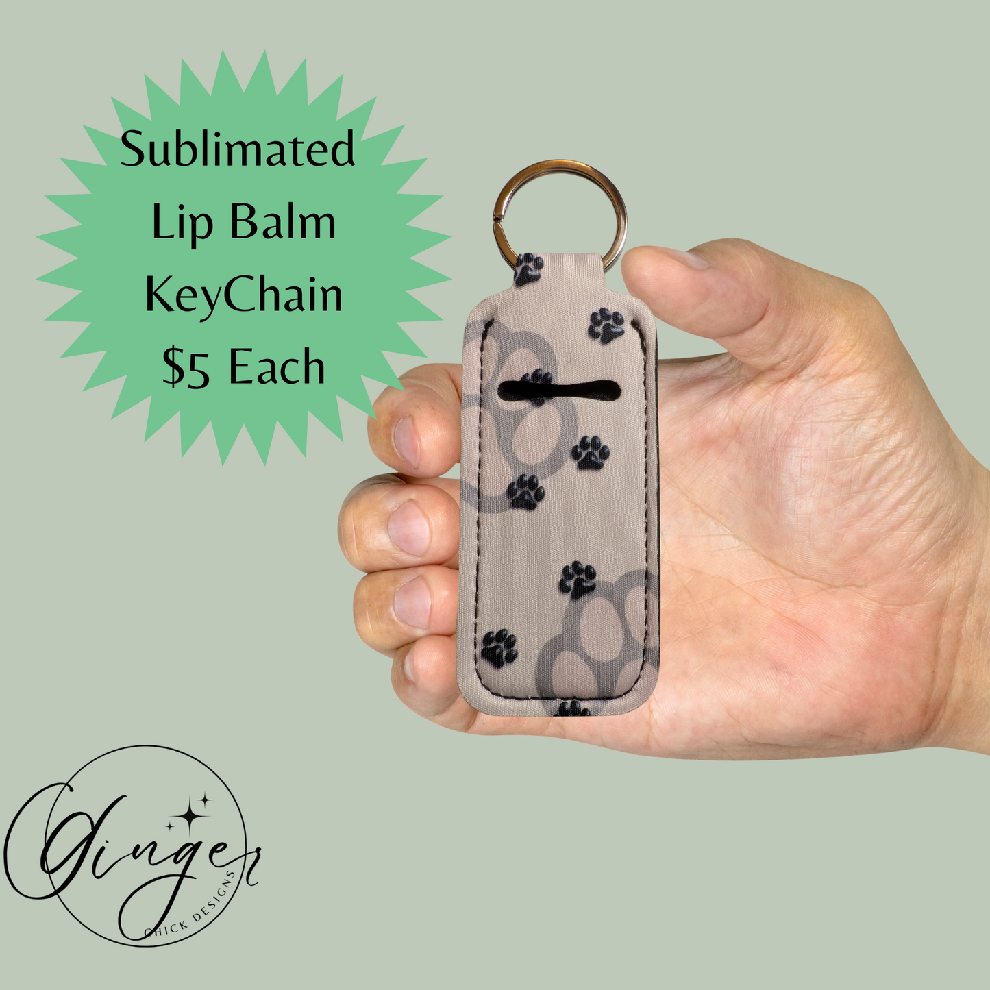 Hand holding a sublimated lip balm keychain with paw prints on a light green background