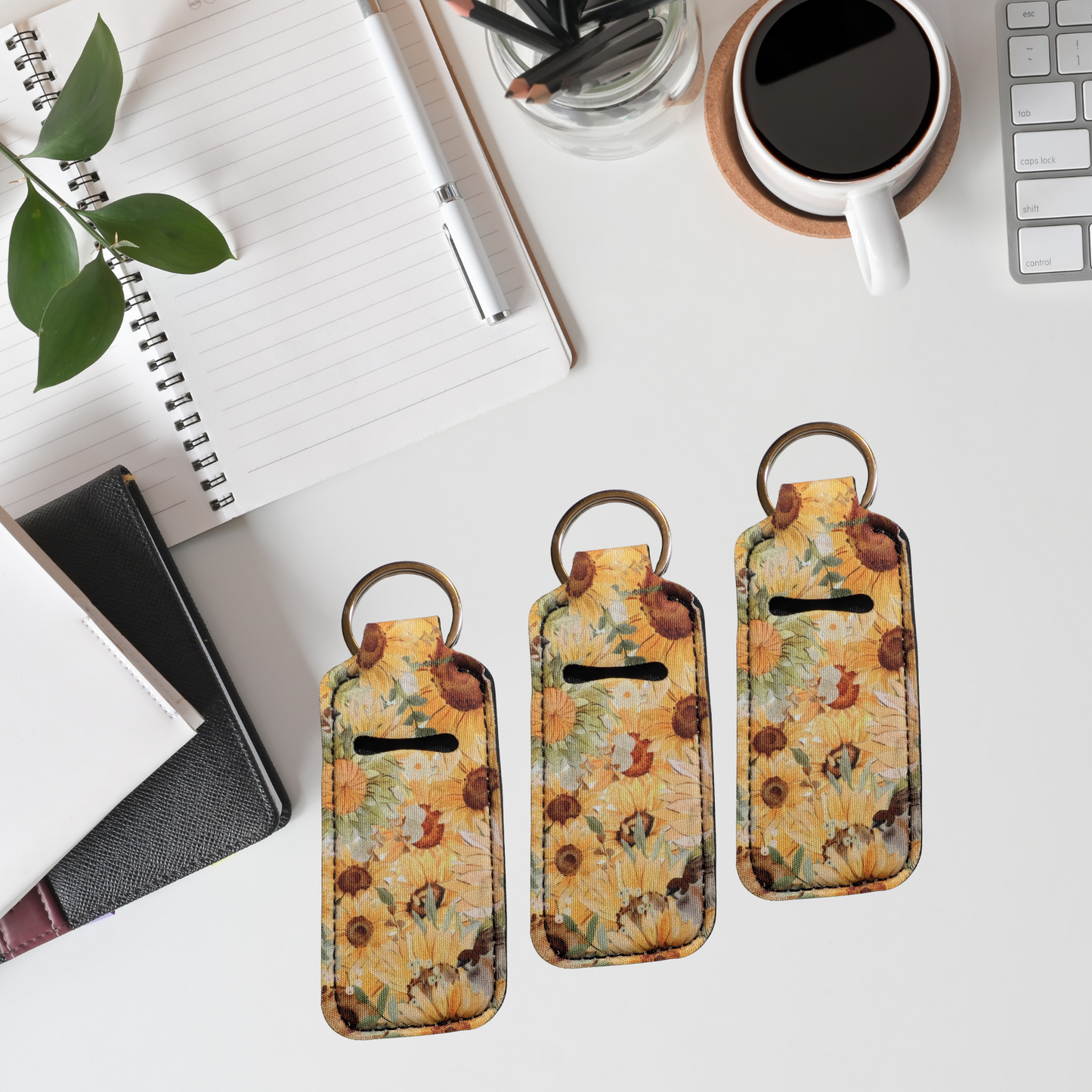Three floral keychains on a desk with a notebook, coffee cup, and plant.