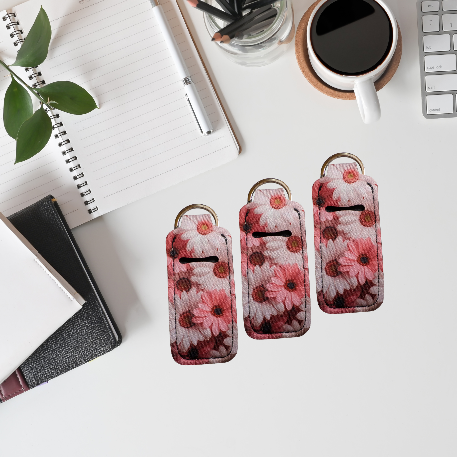 Floral keychains on a desk with a notebook, coffee, and plant.