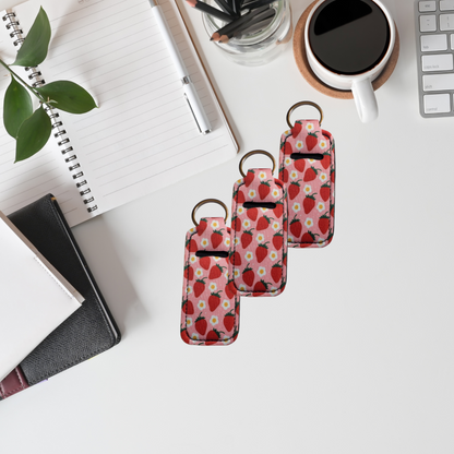 Three strawberry-patterned keychains on a desk with a notebook, coffee cup, and plant.