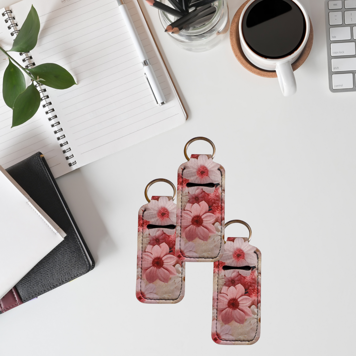 Floral keychain on a desk with a notebook, plant, and coffee cup in the background