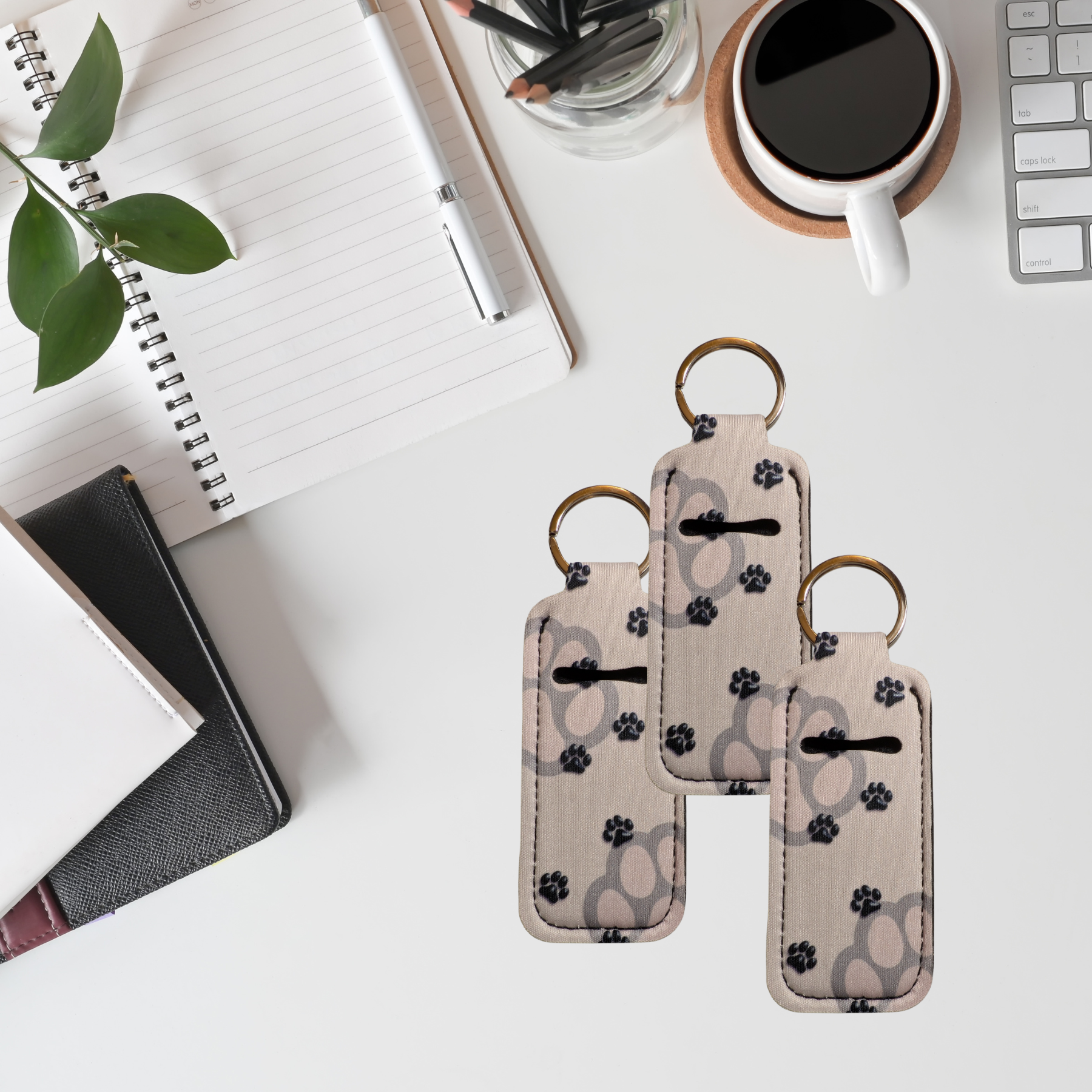Two keychains with paw print pattern on a desk with a notebook, pen, and coffee cup.