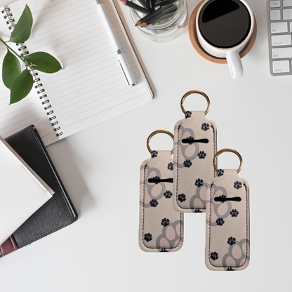 Two keychains with paw print pattern on a desk with a notebook, pen, and coffee cup.