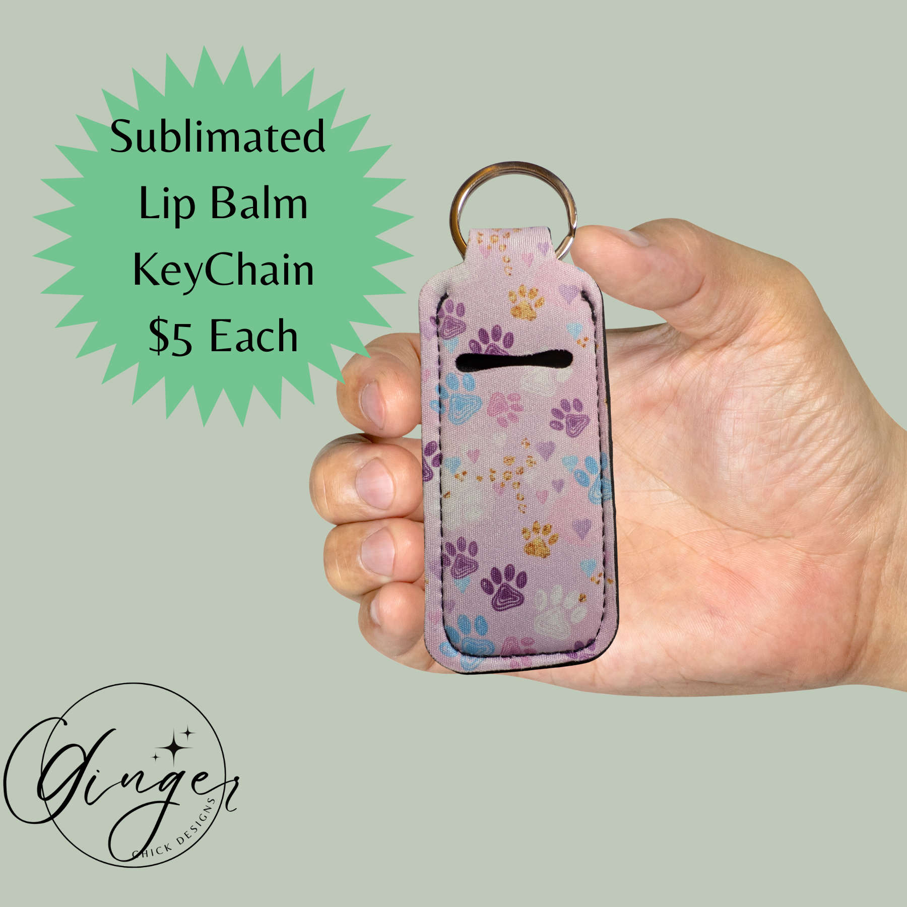 Hand holding a sublimated lip balm keychain with paw print design on a light green background.
