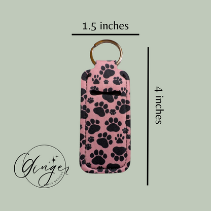 Pink keychain case with black paw prints and dimensions on a light green background