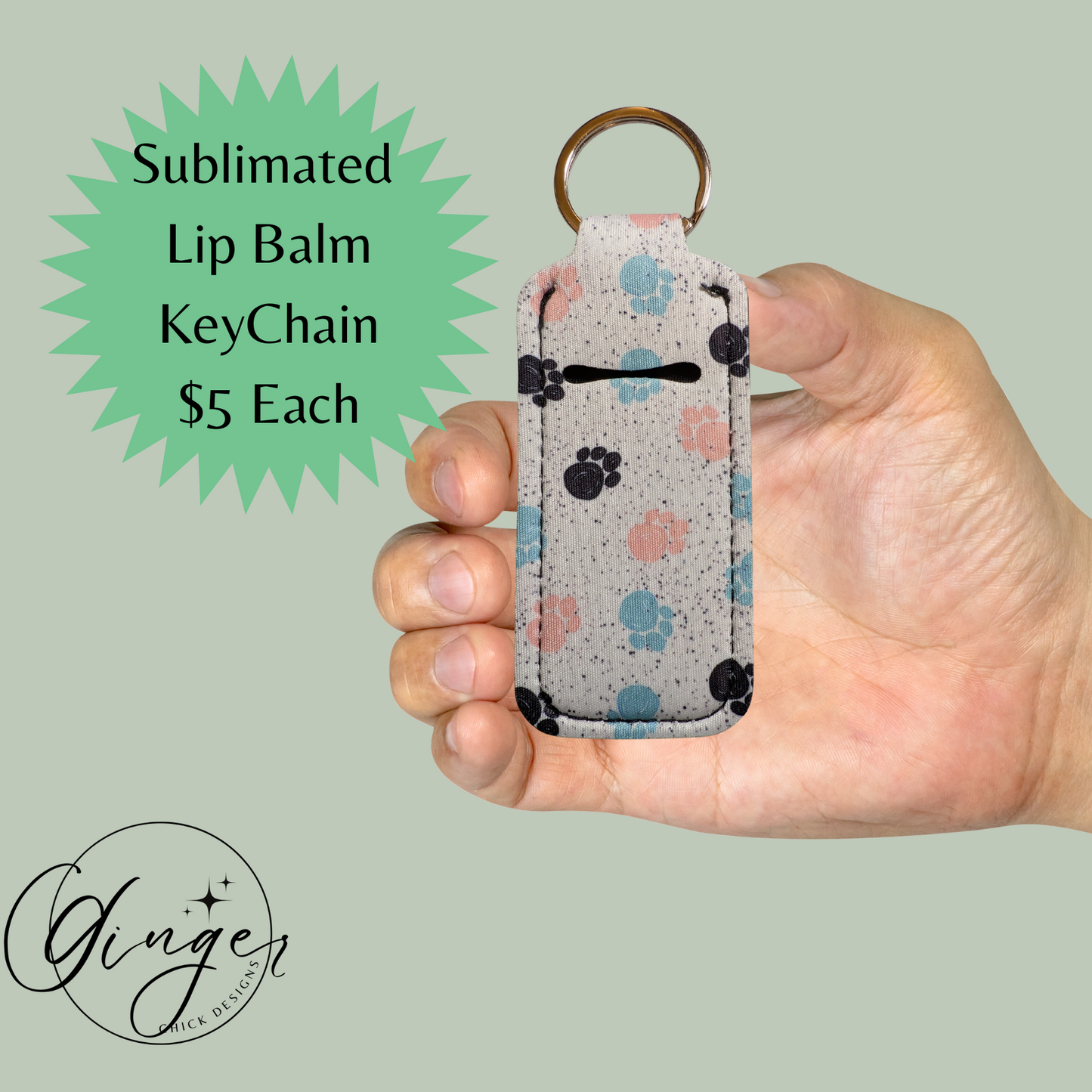 Hand holding a sublimated lip balm keychain with paw print design on a light green background.
