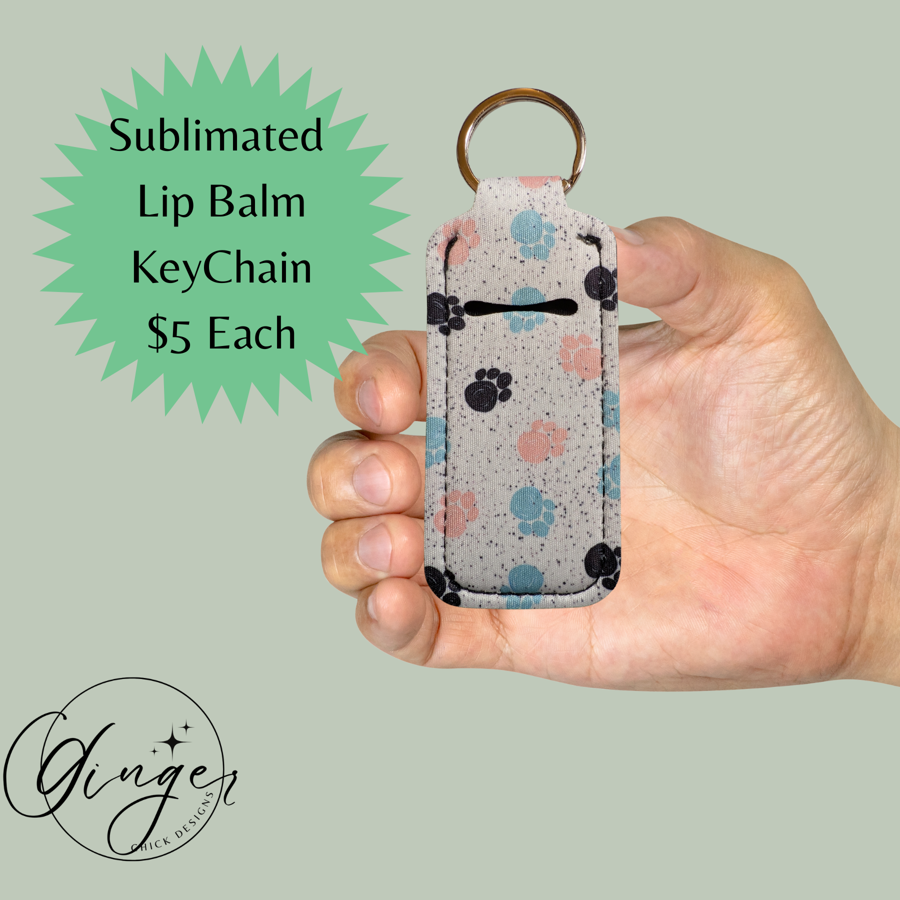 Hand holding a sublimated lip balm keychain with paw print design on a light green background.