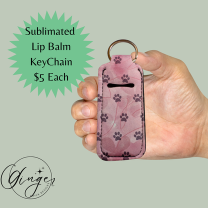 Hand holding a pink lip balm keychain with paw prints on a light green background, featuring text about the product and price.