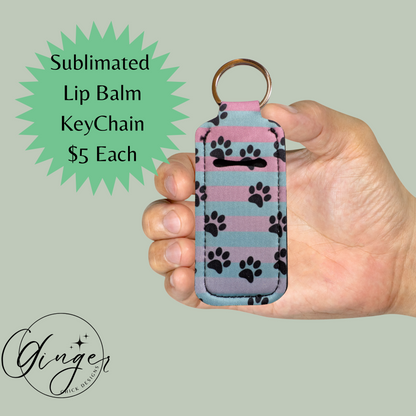 Hand holding a lip balm keychain with paw prints against a light green background
