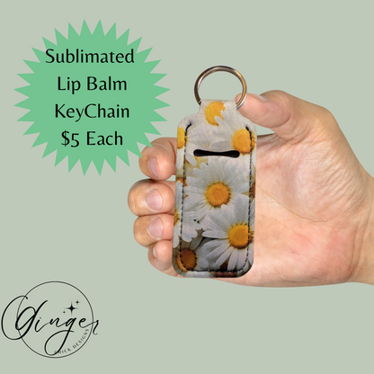 Hand holding a sublimated lip balm keychain with floral design on a light green background